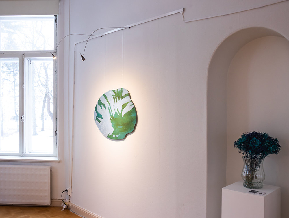 An abstract, oddly shaped painting in light green and blue hanging on an art gallery wall between a window and a vase of flowers
