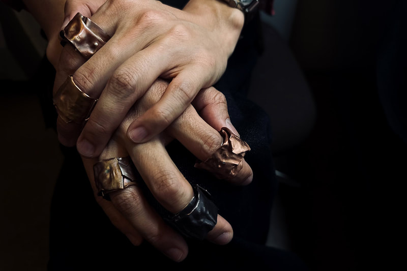 A close view of man's hands wearing a bunch of big silver and copper rings
