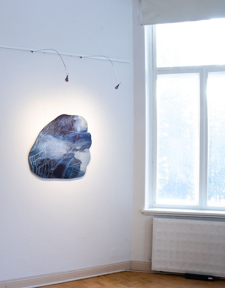 An abstract, oddly shaped acrylic painting in color blue hanging on an art gallery wall next to a window